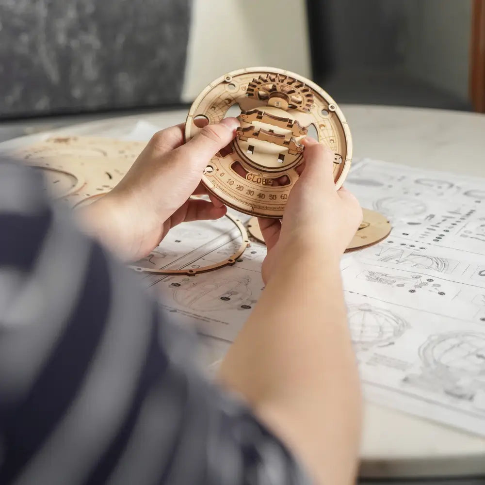 Asamblare puzzle 3D glob luminos Rokr piesele mecanice din lemn fiind conectate conform instructiunilor pentru a crea un glob elegant si functional